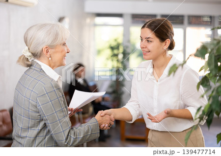 Positive young woman shaking hands with aged female business partner 139477714