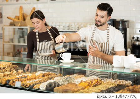 Two cafe workers prepare coffee for a customer 139477770