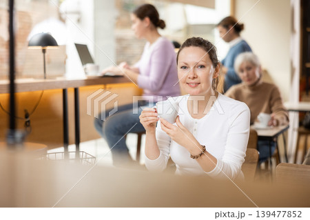 Dreamy woman sitting with cup of coffee in cozy cafe 139477852