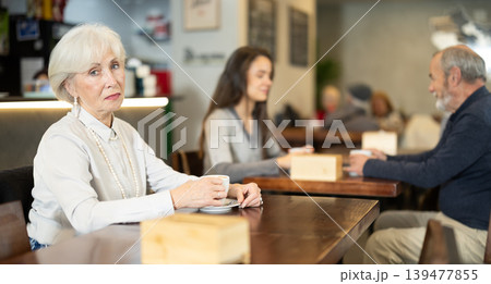Senior woman whiles away time and drink coffee in cafe Senior woman whiles away time and drink coffee in cafe 139477855