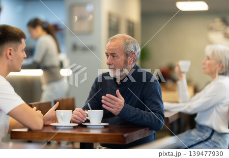 Mature man and her adult son sit together at table in cafe Mature man and her adult son sit together at table in cafe 139477930