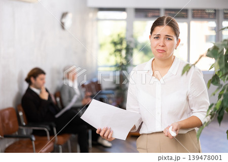Portrait of upset disappointed female office employee holding paper document in hands 139478001