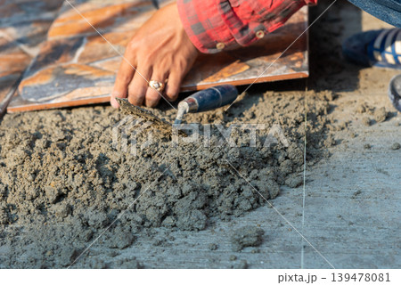 Construction worker installing ceramic floor tiles with cement mortar and hand tools during home renovation and flooring installation process Construction worker installing ceramic floor tiles with cement mortar and hand tools during home renovation and flooring installation process 139478081