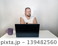 Thoughtful man with scowling face and crossed arms looking critically at a laptop screen, skeptical view 139482560