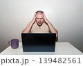 Stressed man clutches his head in shock and anger at an open laptop, experiencing frustration and despair 139482561
