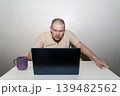 Man peers anxiously and attentively at a laptop monitor, focusing with intensity on a screen 139482562