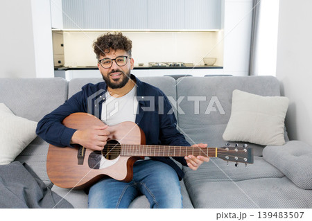 Man playing acoustic guitar on sofa at home Man playing acoustic guitar on sofa at home 139483507