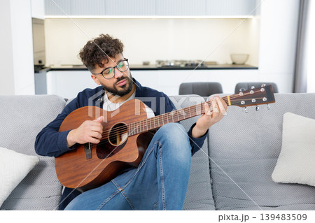 Man playing acoustic guitar and singing on sofa Man playing acoustic guitar and singing on sofa 139483509