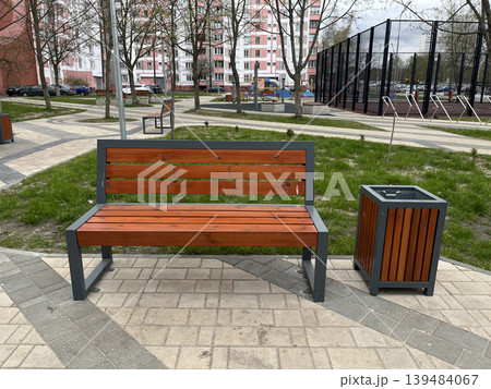 Modern wooden park bench with trash bin in residential courtyard 139484067