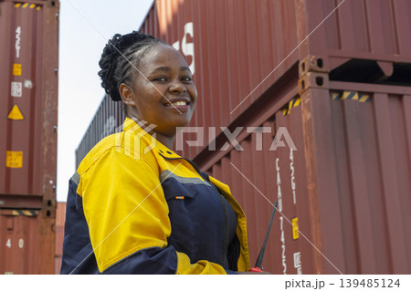 African American female workers in reflective vest and helmet using laptops and radios, standing at container ship yard. African American female workers in reflective vest and helmet using laptops and radios, standing at container ship yard. 139485124