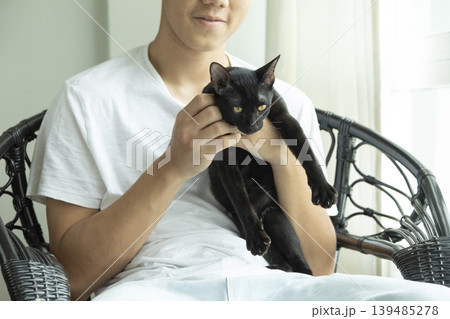 Happy teenage Asian boy holding black cat in white living room. 139485278