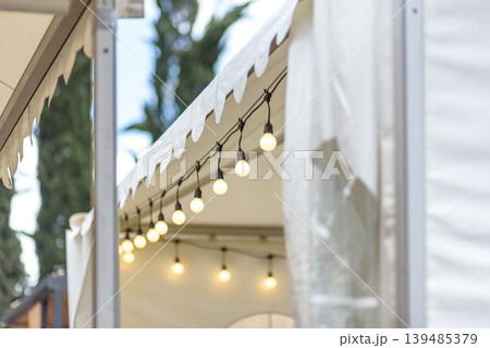 Warm string lights under white canopy tent Warm string lights under white canopy tent 139485379