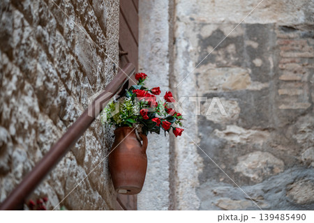 Terracotta vase with red roses on stone wall 139485490