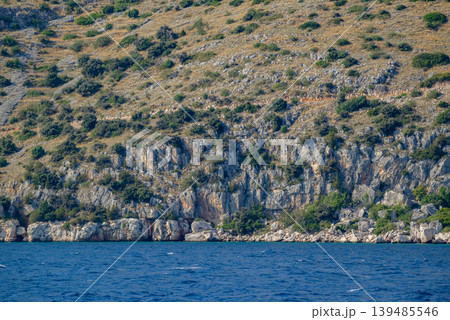 Rocky coastal cliff above calm blue sea Rocky coastal cliff above calm blue sea 139485546