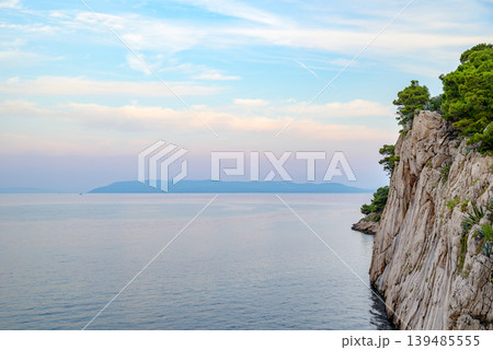 Calm seascape with rocky cliff and distant island 139485555