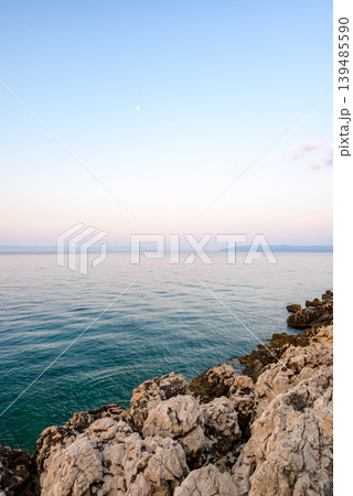 Calm seascape at dusk with rocky coastline and moon 139485590