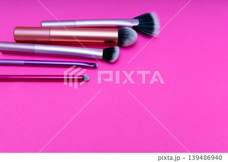 Makeup brushes are spread out on a bright pink surface showing different styles and sizes.  139486940