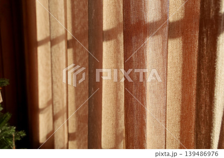 Sunlight filters through sheer curtains in a warm room creating patterns on the wall. Sunlight filters through sheer curtains in a warm room creating patterns on the wall. 139486976
