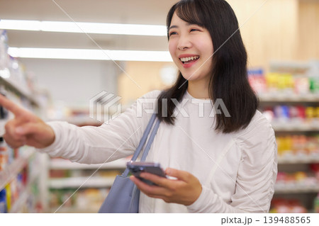 スーパーマーケットでスマホメモを見ながら買い物をする若い女性 スーパーマーケットでスマホメモを見ながら買い物をする若い女性 139488565