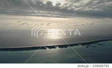 Sunlight reflects calm ocean water near tropical island with overwater bungalows, creating beautiful serene scene under cloudy sunset sky. Exotic travel vacation getaway background. Drone flight Sunlight reflects calm ocean water near tropical island with overwater bungalows, creating beautiful serene scene under cloudy sunset sky. Exotic travel vacation getaway background. Drone flight 139488785