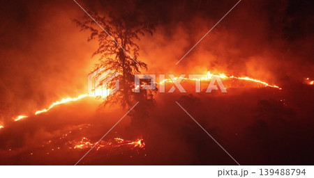 Forest wildfire at night, bright orange flames and heavy smoke consuming trees and landscape, dramatic aerial view highlighting environmental destruction and climate crisis. Aerial drone panorama Forest wildfire at night, bright orange flames and heavy smoke consuming trees and landscape, dramatic aerial view highlighting environmental destruction and climate crisis. Aerial drone panorama 139488794