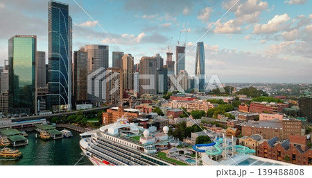 Sydney skyline aerial view urban cityscape. Modern skyscrapers buildings and large cruise ship docked at bustling Circular Quay harbor. Contrasting new and old architecture under bright evening sky Sydney skyline aerial view urban cityscape. Modern skyscrapers buildings and large cruise ship docked at bustling Circular Quay harbor. Contrasting new and old architecture under bright evening sky 139488808
