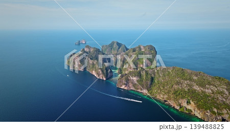 Tropical Phi Phi island displaying lush green limestone cliffs rising from turquoise water with boat cruising past, offering a stunning travel destination and vacation landscape. Aerial drone panorama 139488825