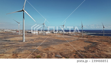 Tenerife: Wind farm turbines generating clean, sustainable power on a coastal landscape, with industrial structures and the blue Atlantic Ocean under a clear sky, Canary Islands. Drone flight Tenerife: Wind farm turbines generating clean, sustainable power on a coastal landscape, with industrial structures and the blue Atlantic Ocean under a clear sky, Canary Islands. Drone flight 139488851