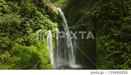 Sendang Gile waterfall cascading into a lush tropical rainforest. Surrounded by vibrant green vegetation. With people standing in the refreshing natural pool. Highlighting peace and nature beauty 139488856