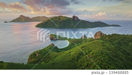 Fiji, Yasawa tropical Islands with lush green mountains hills, white beach and calm turquoise lagoon water under vibrant sunset sky, idyllic South Pacific paradise. Aerial view drone flight panorama Fiji, Yasawa tropical Islands with lush green mountains hills, white beach and calm turquoise lagoon water under vibrant sunset sky, idyllic South Pacific paradise. Aerial view drone flight panorama 139488885