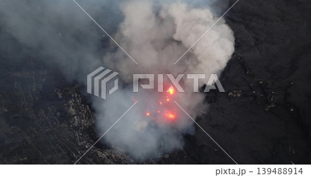 Mount Yasur volcano erupting from an aerial drone viewpoint, showing molten lava explosions and thick smoke rising from the active crater in a dramatic display of raw power and natural hazard Mount Yasur volcano erupting from an aerial drone viewpoint, showing molten lava explosions and thick smoke rising from the active crater in a dramatic display of raw power and natural hazard 139488914