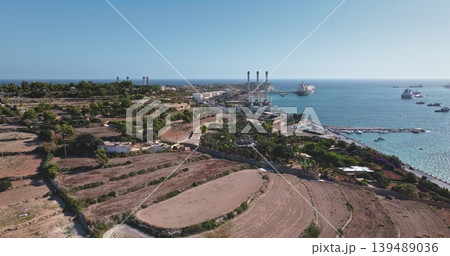 Malta: Aerial view capturing Delimara Power Station in Marsaxlokk, Malta, featuring the power plant, fuel storage tanks, and cargo ships in the Mediterranean Sea. Drone flight Malta: Aerial view capturing Delimara Power Station in Marsaxlokk, Malta, featuring the power plant, fuel storage tanks, and cargo ships in the Mediterranean Sea. Drone flight 139489036