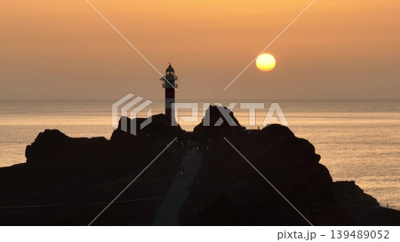 Tourists enjoy Punta de Teno Lighthouse at sunset in Tenerife, Canary Islands, Spain. Rocky landscape silhouette bright orange sky. Travel destination. Nature background. Drone flight panorama Tourists enjoy Punta de Teno Lighthouse at sunset in Tenerife, Canary Islands, Spain. Rocky landscape silhouette bright orange sky. Travel destination. Nature background. Drone flight panorama 139489052
