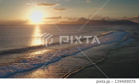 Breathtaking aerial view of a golden sunset casting a warm glow over gentle ocean waves, with a tranquil tropical island in the distance, creating a serene and idyllic vacation scene 139489078