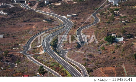 Tenerife, Canary Islands: Aerial view of cars navigating TF-1 highway through Tenerife's volcanic terrain, highlighting unique infrastructure transportation and natural scenery. Drone flight Tenerife, Canary Islands: Aerial view of cars navigating TF-1 highway through Tenerife's volcanic terrain, highlighting unique infrastructure transportation and natural scenery. Drone flight 139489141