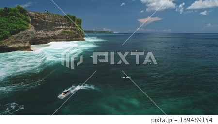 Turquoise ocean waves rolling toward the shore, surfers riding the swells, and steep cliffs with lush greenery under a sunny blue sky at Dreamland Beach, Bali Turquoise ocean waves rolling toward the shore, surfers riding the swells, and steep cliffs with lush greenery under a sunny blue sky at Dreamland Beach, Bali 139489154