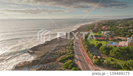 Portugal, Lisbon: Cascais coastline at sunrise. Breathtaking aerial view of winding road and rocky coast. Luxurious villas among lush greenery. Travel destination. Drone 139489173