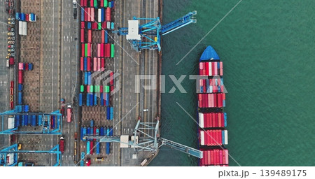 Container ship docked at busy global shipping port, showing cranes loading and unloading multicolored cargo containers, international freight transport logistics. Aerial view drone shot, top down Container ship docked at busy global shipping port, showing cranes loading and unloading multicolored cargo containers, international freight transport logistics. Aerial view drone shot, top down 139489175
