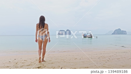 Ko Lanta, Thailand: Beautiful young woman in bikini walk sandy beach, clear turquoise water, longtail boat and iconic limestone islands in background, tropical summer vacation and travel Ko Lanta, Thailand: Beautiful young woman in bikini walk sandy beach, clear turquoise water, longtail boat and iconic limestone islands in background, tropical summer vacation and travel 139489186