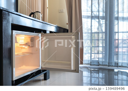 A small refrigerator sits beneath a wooden desk with chair, creating a clean hotel room setup that supports minibar service and compact guest comfort. A small refrigerator sits beneath a wooden desk with chair, creating a clean hotel room setup that supports minibar service and compact guest comfort. 139489496