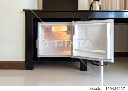 A small refrigerator sits beneath a wooden desk with chair, creating a clean hotel room setup that supports minibar service and compact guest comfort. A small refrigerator sits beneath a wooden desk with chair, creating a clean hotel room setup that supports minibar service and compact guest comfort. 139489497