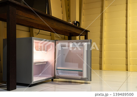 A small refrigerator sits beneath a wooden desk with chair, creating a clean hotel room setup that supports minibar service and compact guest comfort. A small refrigerator sits beneath a wooden desk with chair, creating a clean hotel room setup that supports minibar service and compact guest comfort. 139489500
