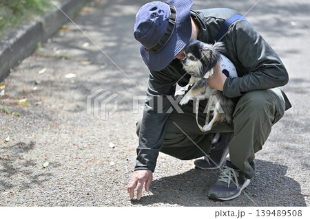 愛犬とお散歩　温度は大丈夫かな？　地面の温度を手で確認する男性　 139489508