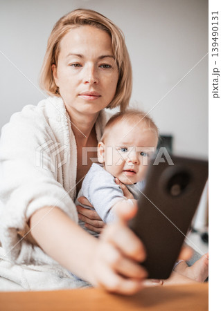 Authentic shot of neo mother and her newborn baby making a video call to father or relatives with laptop on a sofa in a living room. Authentic shot of neo mother and her newborn baby making a video call to father or relatives with laptop on a sofa in a living room. 139490131