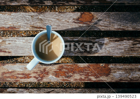a cup of coffee on wooden bench in shade of morning sunrise with tea spoon looked like  7 o'clock's wall clock 139490523