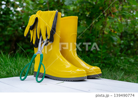 Yellow garden boots with bucket and gardening shovel on green grass outdoor background. Copy space. Garden tools in rural cottagecore lifestyle countryside living organic sustainable Yellow garden boots with bucket and gardening shovel on green grass outdoor background. Copy space. Garden tools in rural cottagecore lifestyle countryside living organic sustainable 139490774