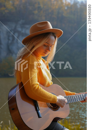 Blonde woman playing string guitar outdoors in autumn forest. Concept of sound therapy, mental health and wellness rituals. Calmness tranquility audio-sensory practices. Aura farming energy Blonde woman playing string guitar outdoors in autumn forest. Concept of sound therapy, mental health and wellness rituals. Calmness tranquility audio-sensory practices. Aura farming energy 139490880