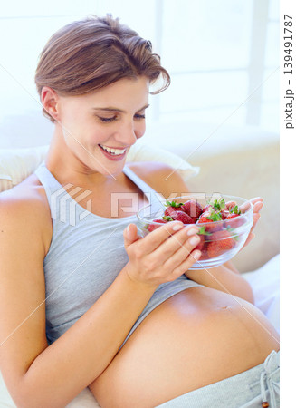 Pregnant woman, strawberry and nutrition in bedroom with relax wellness for eating fruit in house. Young person, happy and prenatal health diet with natural food for vitamins and care in apartment 139491787