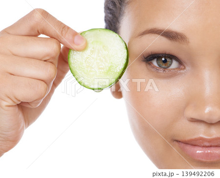 Skincare, cucumber and woman face or eye beauty for cosmetics, natural product and Vitamin C makeup in studio. Portrait of a young, happy model with green fruit and dermatology on a white background Skincare, cucumber and woman face or eye beauty for cosmetics, natural product and Vitamin C makeup in studio. Portrait of a young, happy model with green fruit and dermatology on a white background 139492206