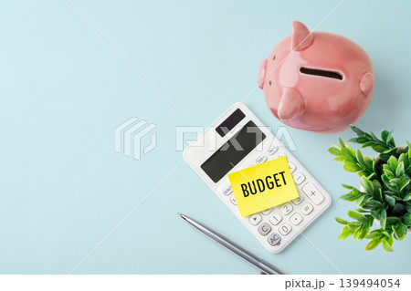 Piggy bank with calculator and budget note on light blue background, concept for financial planning, personal budgeting, and saving money, top view Piggy bank with calculator and budget note on light blue background, concept for financial planning, personal budgeting, and saving money, top view 139494054